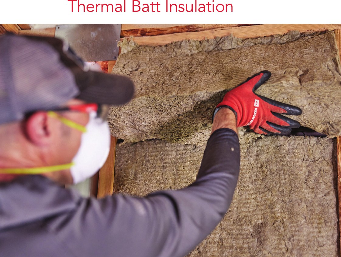 An installer fitting a stone wool batt around an electrical box in a stud bay