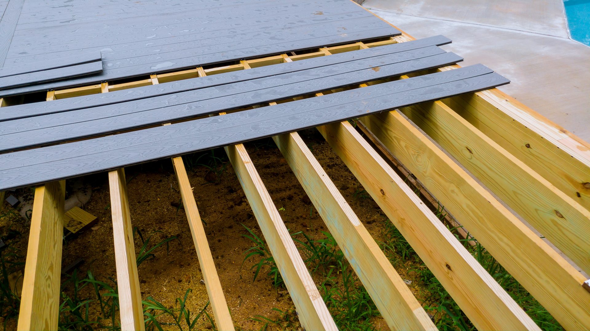 Composite deck boards being installed over treated lumber joists at a backyard build